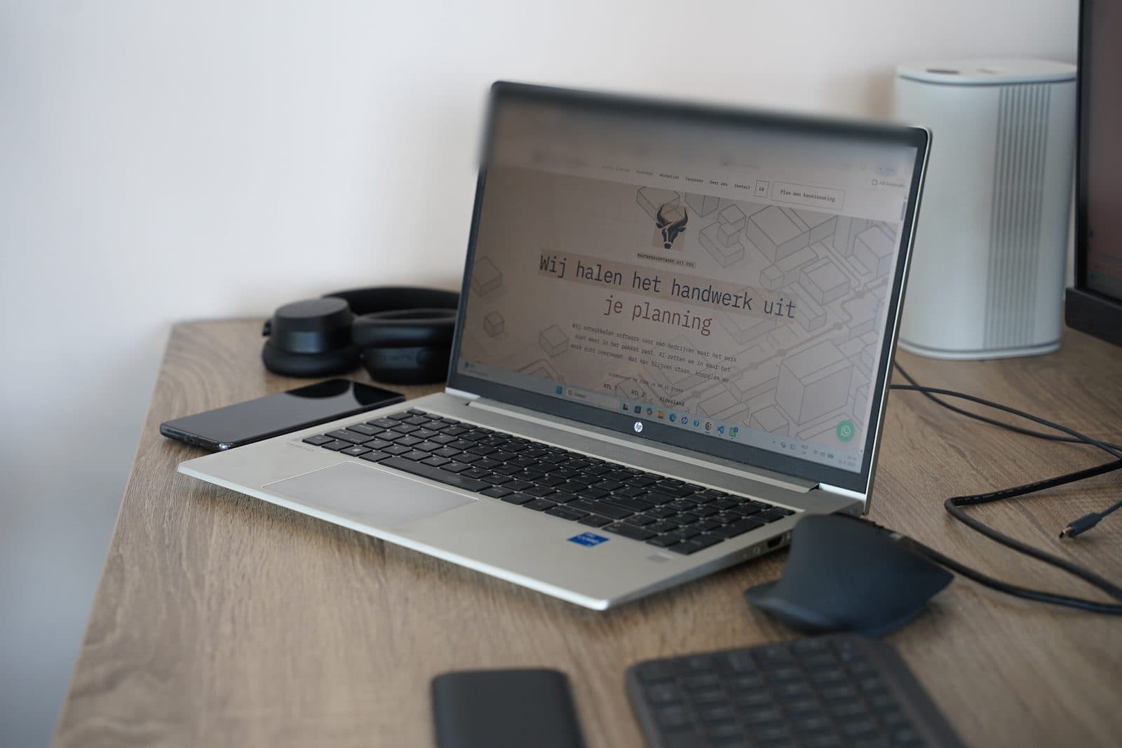 Een opengeklapte laptop op een bureau met een eerste versie van een website, met een koptelefoon en telefoon ernaast