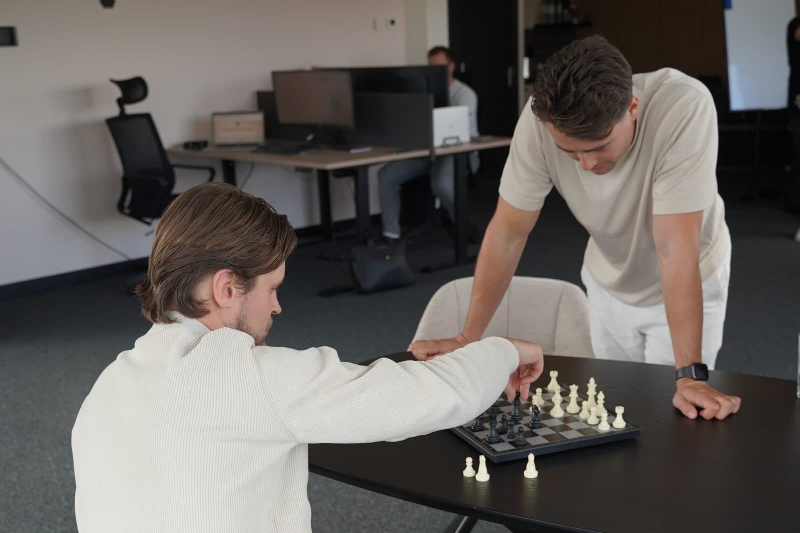Twee collega's schaken aan een tafel op het kantoor van Elusive, de één zittend, de ander over het bord gebogen